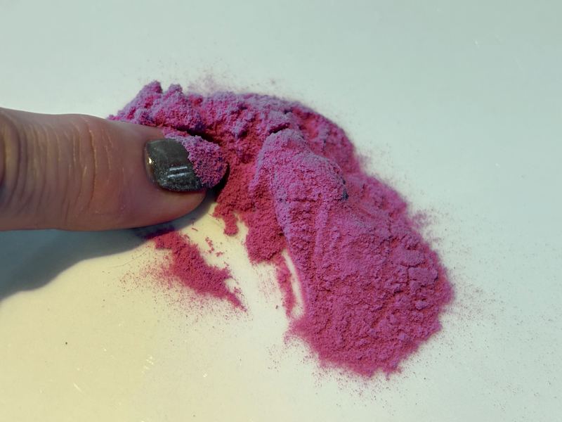A fingertip touching a small pile of bright pink dragon fruit powder on a white surface